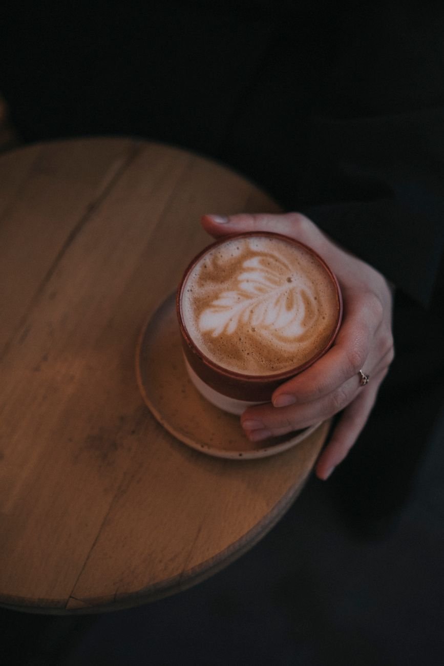 A hand holding a coffee cup with latte art in a cosy café setting